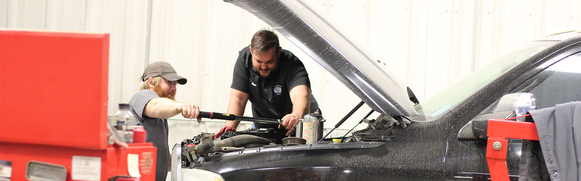 Two technicians working on diesel engine of black pickup truck